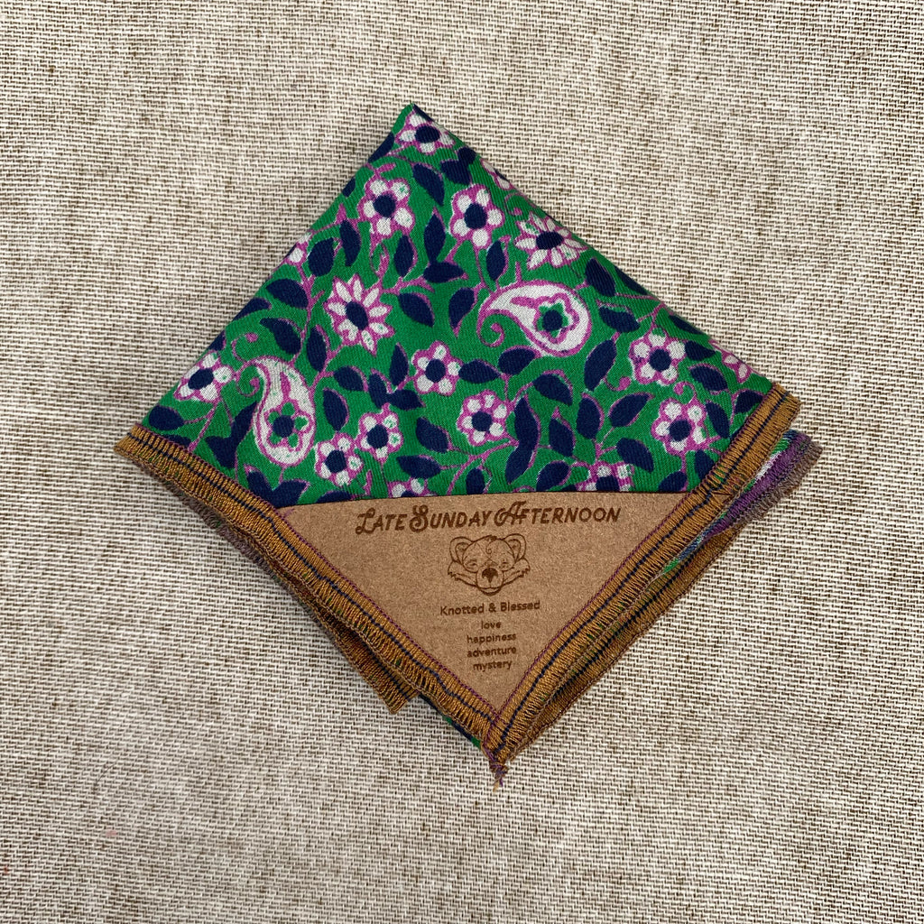 a pocket square folded showing a green and purple floral motif with a small brown tag in the corner 