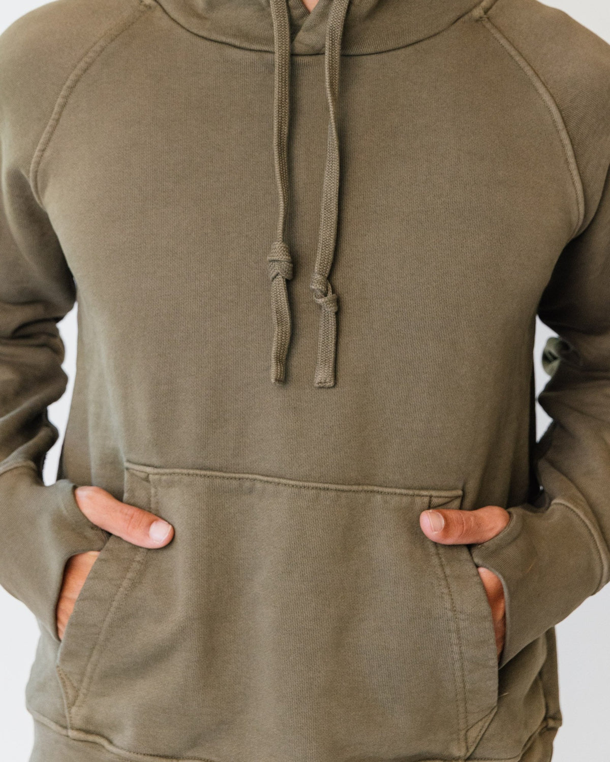 Hands in the front pouch of an olive Apollo X hoodie