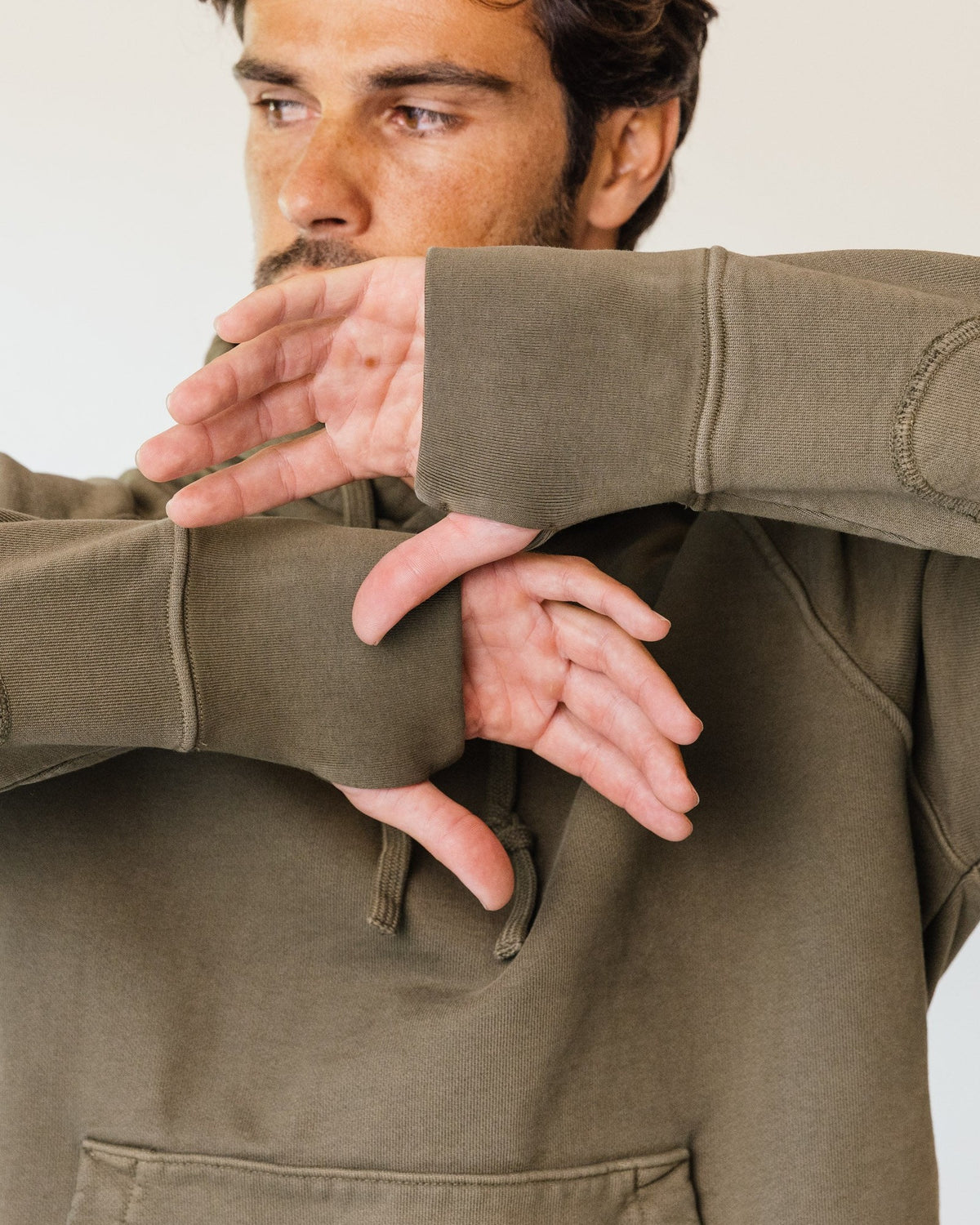 Thumbs through the thumb hole cuffs of an olive Apollo X hoodie