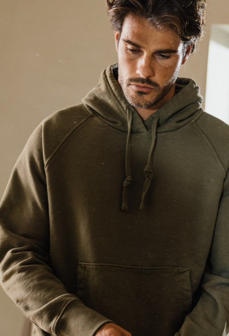 A man in an olive Apollo X hoodie, looking down in a quiet room