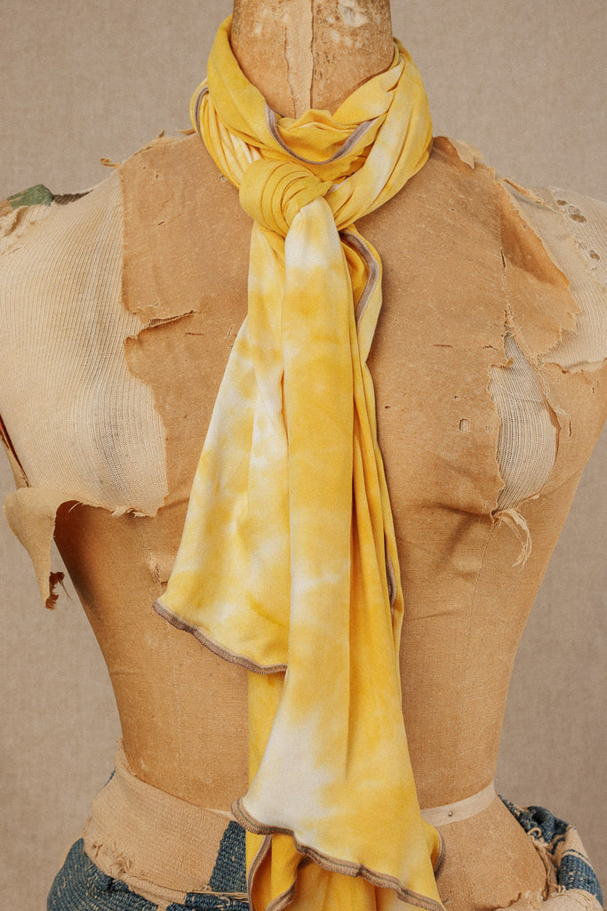 closeup of a bright yellow tie dye scarf wrapped around the neck of a mannequin and tied in a knot