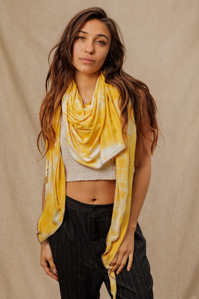 a woman wearing a a bright yellow tie dye scarf draped around her neck