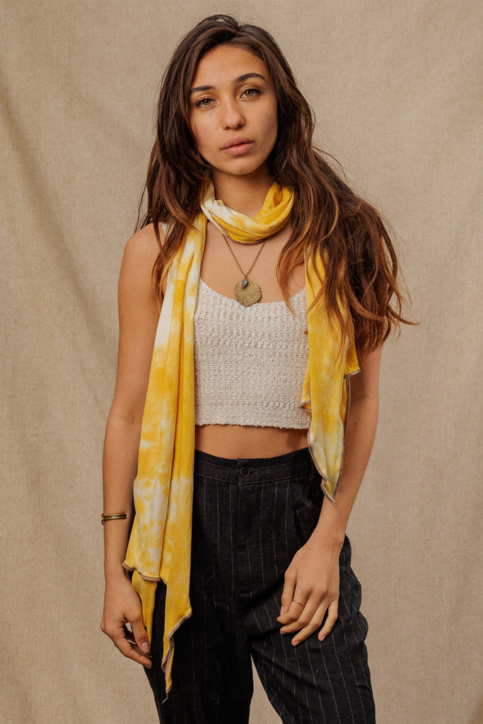 a woman wearing a a bright yellow tie dye scarf wrapped around her neck