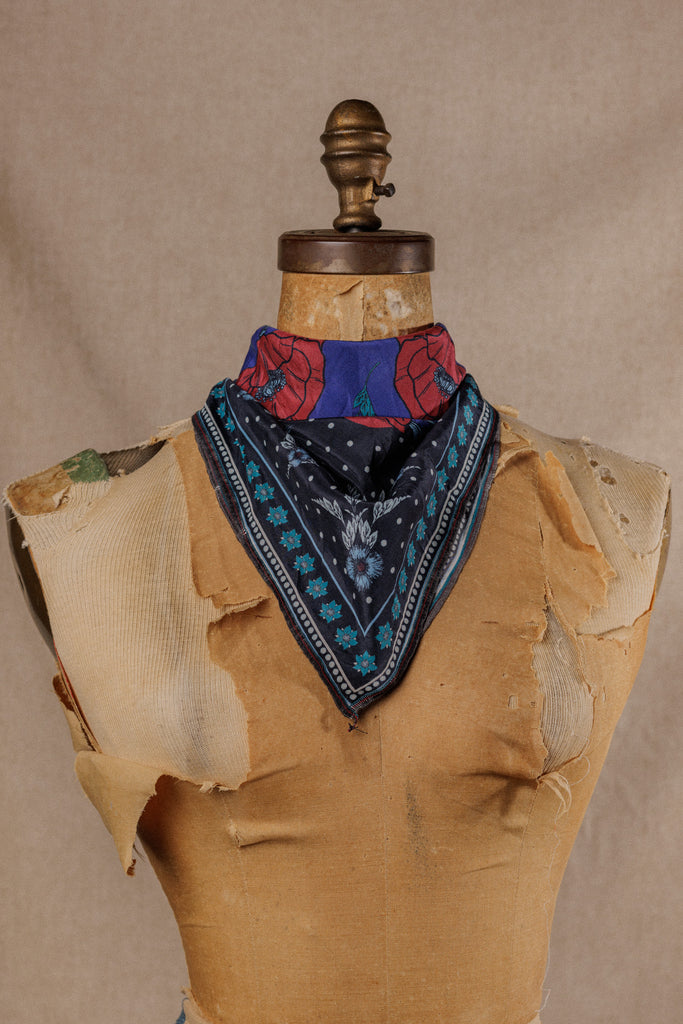 a bandana with a black, blue and white motif on the bottom and on top bright red poppies on a purple background, displayed around the neck of a mannequin