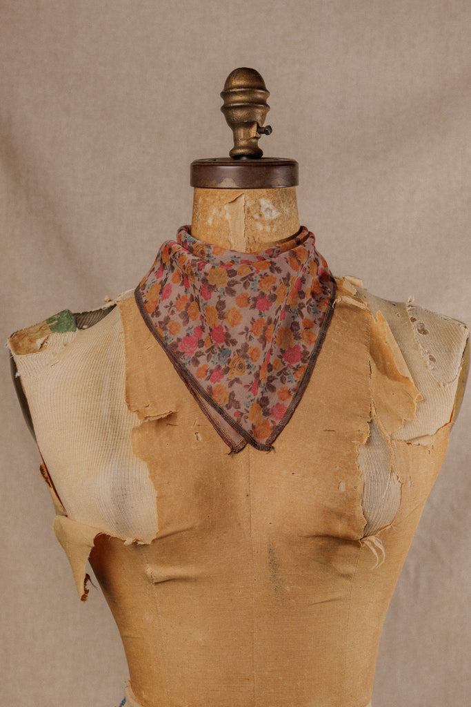a bandana with warm colored floral and brown motif displayed on the neck of a mannequin