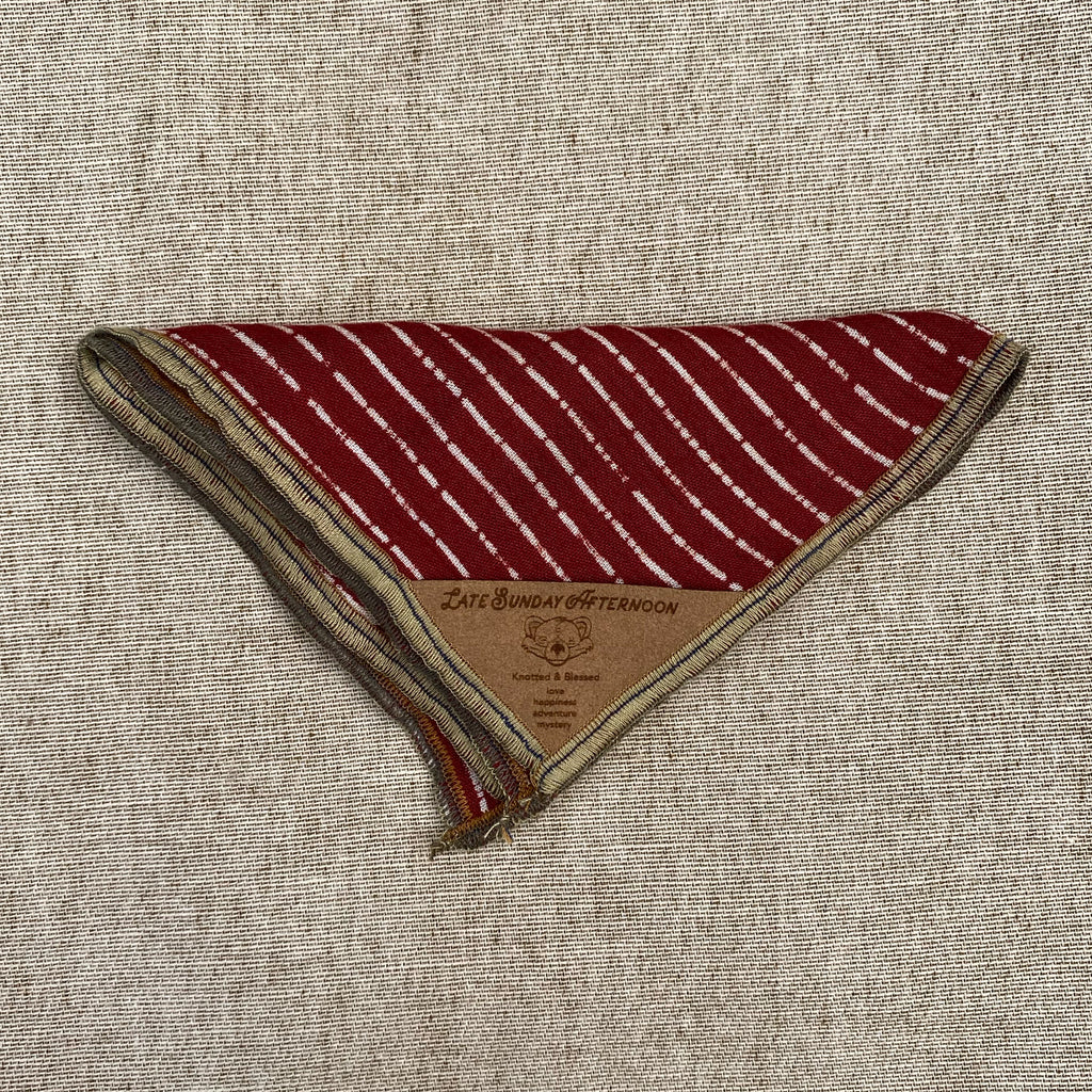 a pocket square folded triangularly, a burgundy and white stripe motif with a brown tag with an image of a bear