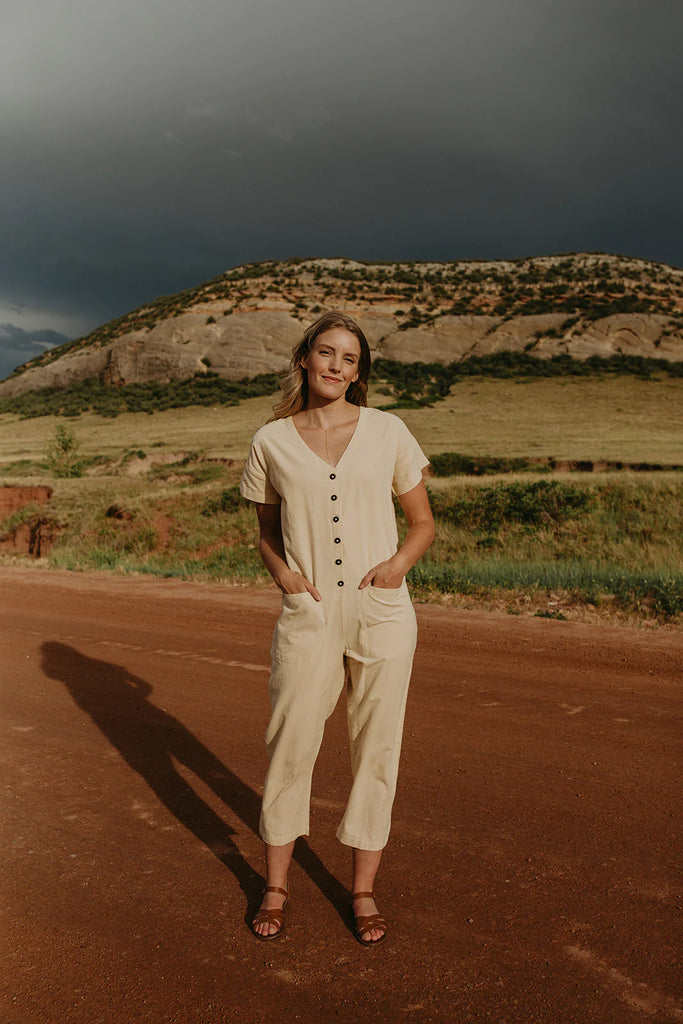 a girl wearing a white short sleeve jumpsuit with buttons down the front and pockets