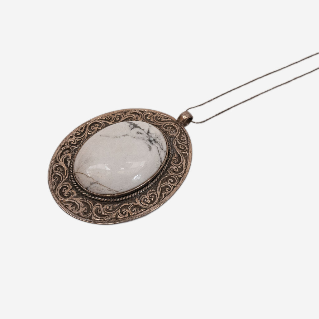 a silver pendant with details and a large white stone on a chain