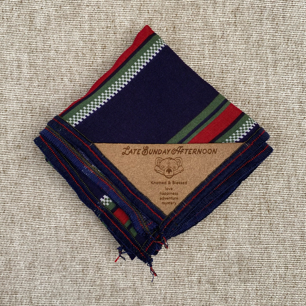 a pocket square folded showing a navy, red, green, and white motif, a brown tag with an image of a bear in the bottom corner