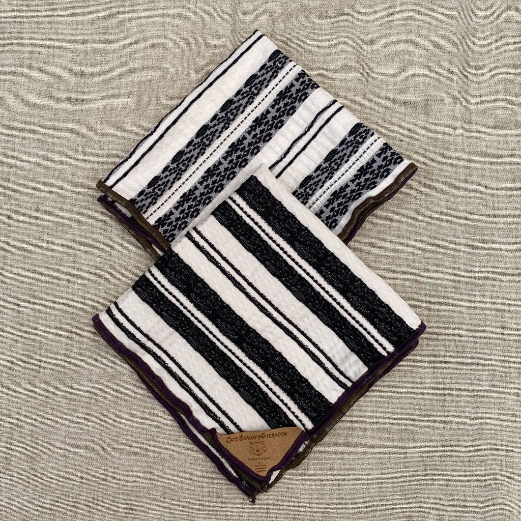 two of the same handkerchief shown folded to display both reversible patterns; black and white stripe motifs