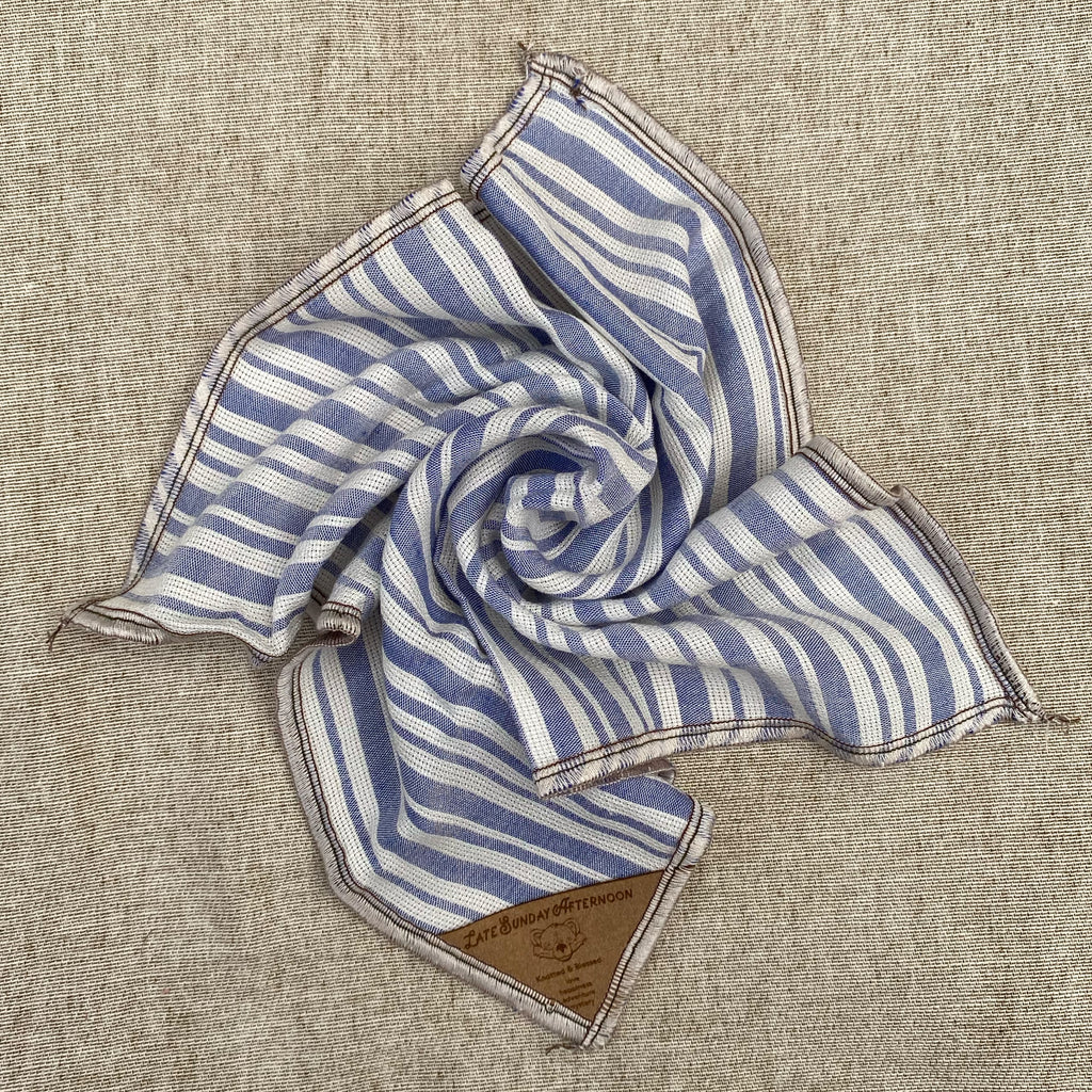 a pocket square showing a pale blue and white stripe motif with a small brown tag in a corner
