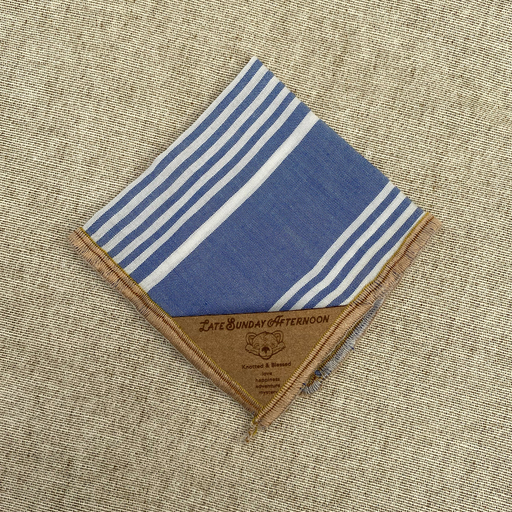 a folded pocket square showing a pale blue and white stripe motif with a small brown tag in a corner