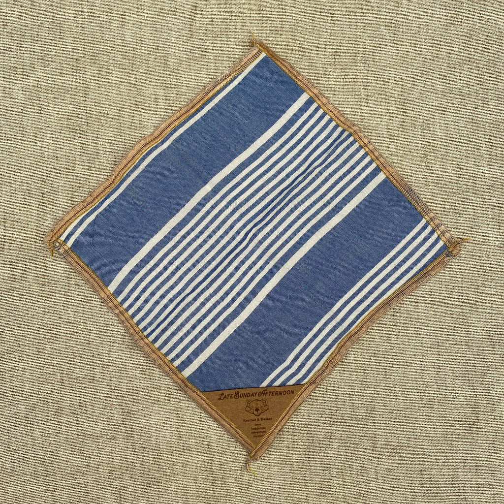 an open pocket square showing a pale blue and white stripe motif with a small brown tag in a corner