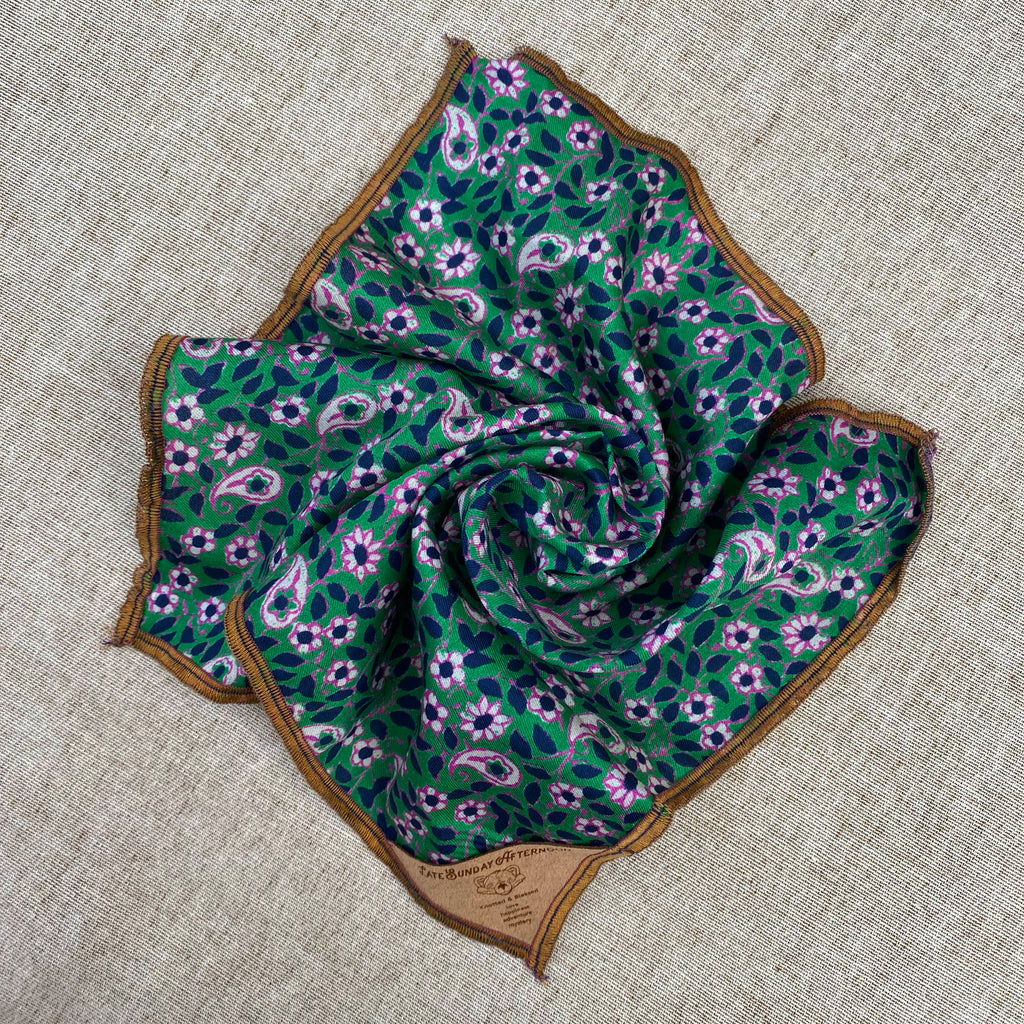 a pocket square open showing a green and purple floral motif with a small brown tag in the corner